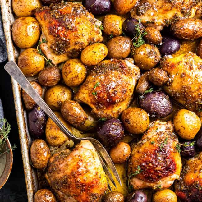 baked honey mustard chicken thighs and potatoes on a baking sheet with a fork.