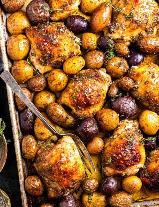 baked honey mustard chicken thighs and potatoes on a baking sheet with a fork.