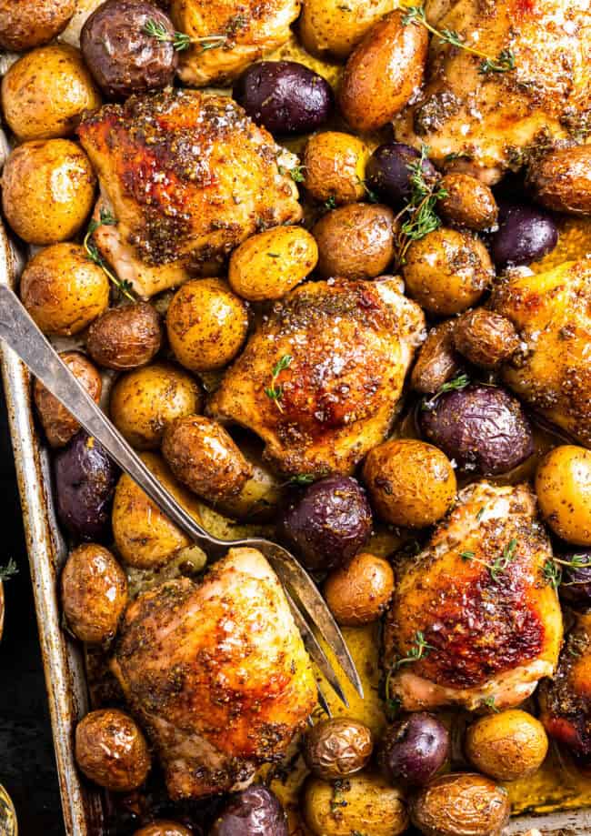 baked honey mustard chicken thighs and potatoes on a baking sheet with a fork.