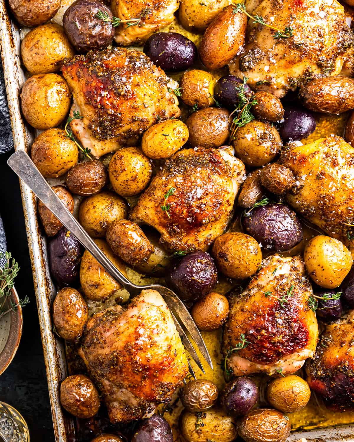 baked honey mustard chicken thighs and potatoes on a baking sheet with a fork.