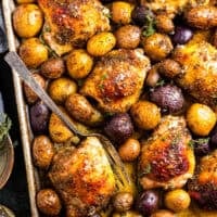 baked honey mustard chicken thighs and potatoes on a baking sheet with a fork.