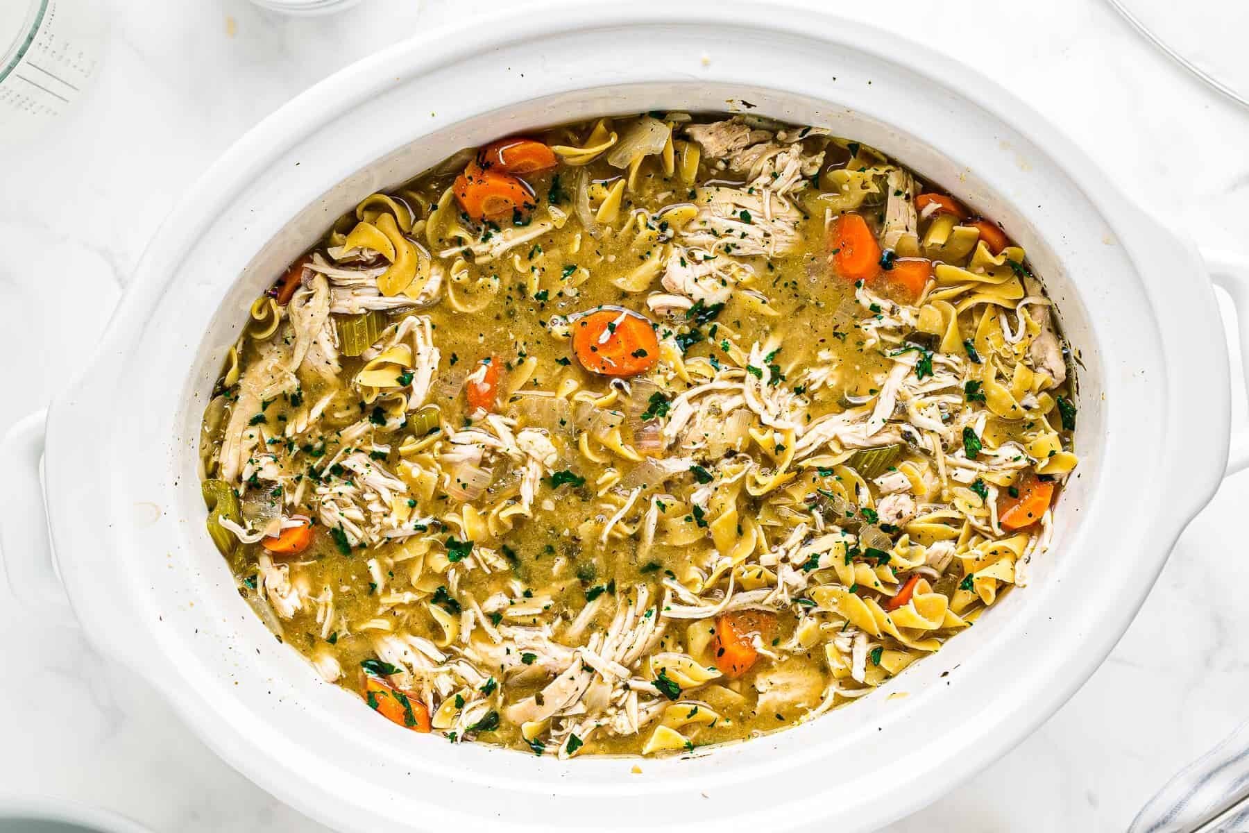 chicken noodle soup in a white crockpot