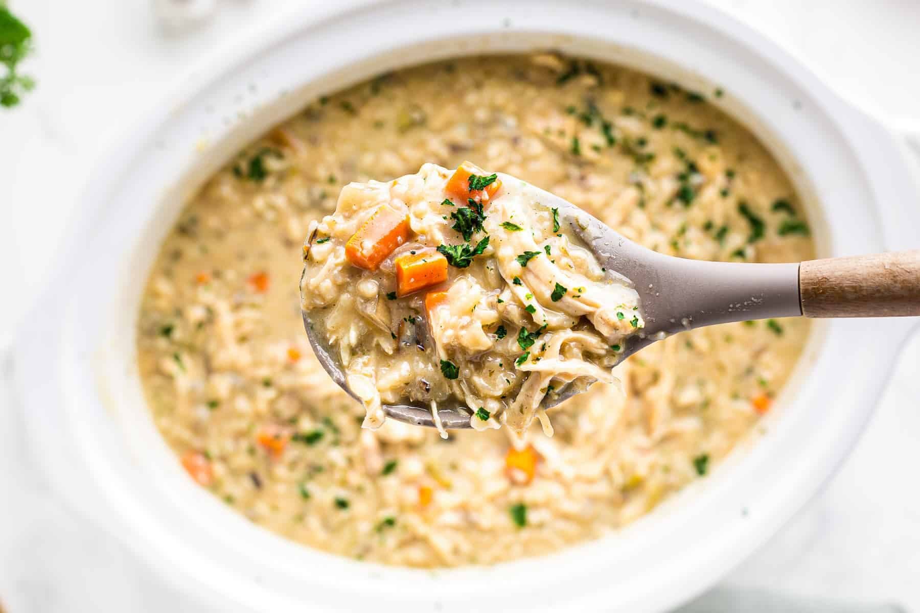 A spoonful of chicken and wild rice soup held above a slow cooker.