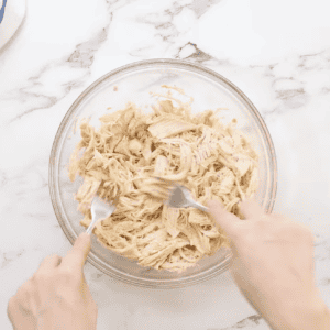 shredding chicken with 2 forks in a glass bowl.