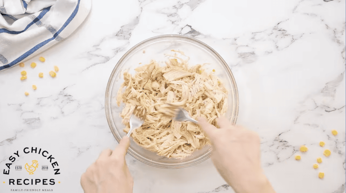 shredding chicken with 2 forks in a glass bowl.