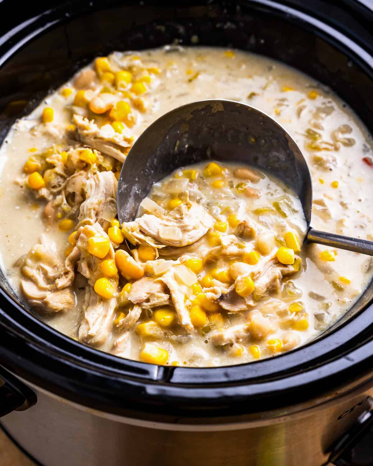 a ladle scooping white chicken enchilada soup from a crockpot.