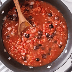 olive and tomato sauce in a frying pan with a wooden spoon.