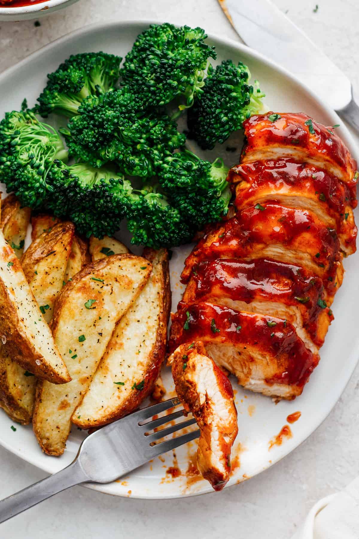 sliced bbq chicken breast on plate with broccoli and potato wedges