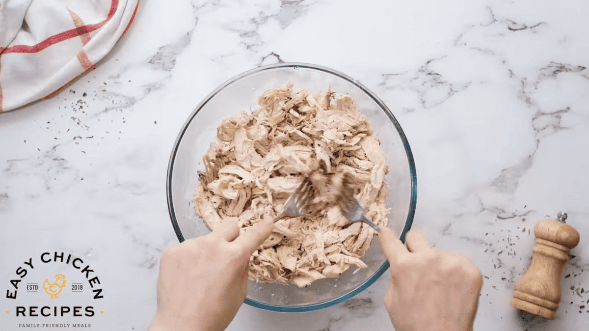 Chicken is being shredded in a bowl with two forks. 