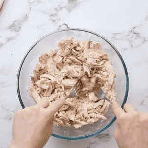 Chicken is being shredded in a bowl with two forks.
