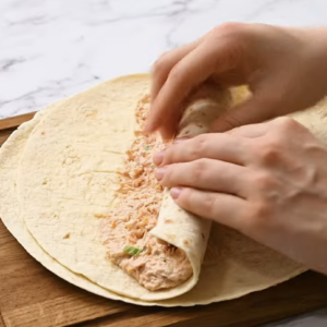 A tortilla is being rolled up with creamy chicken filling.