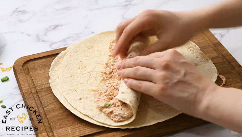 A tortilla is being rolled up with creamy chicken filling.