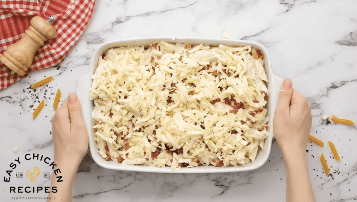 A casserole dish is filled with pasta and topped with bacon and cheese. 