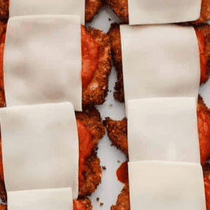 breaded fried chicken thighs topped with marinara sauce and cheese slices in a baking dish.