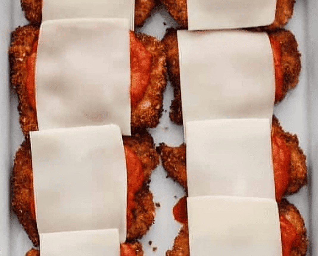 breaded fried chicken thighs topped with marinara sauce and cheese slices in a baking dish.