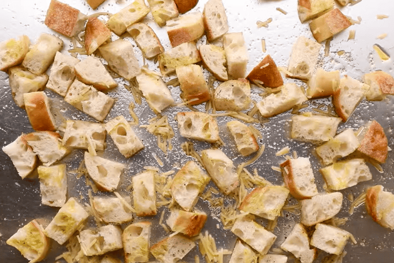 Chopped Italian bread, olive oil, Parmesan, and seasonings on a baking sheet.