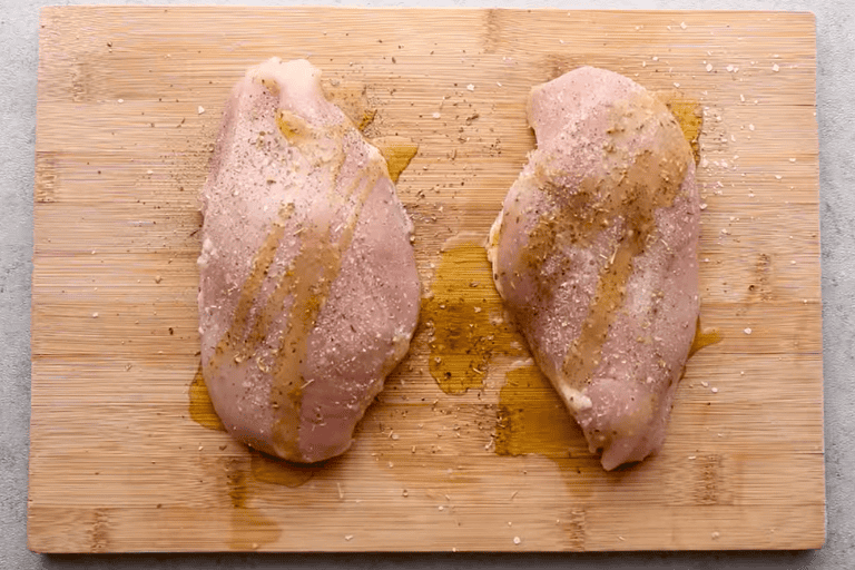 Two seasoned chicken breasts on a wooden chopping board.