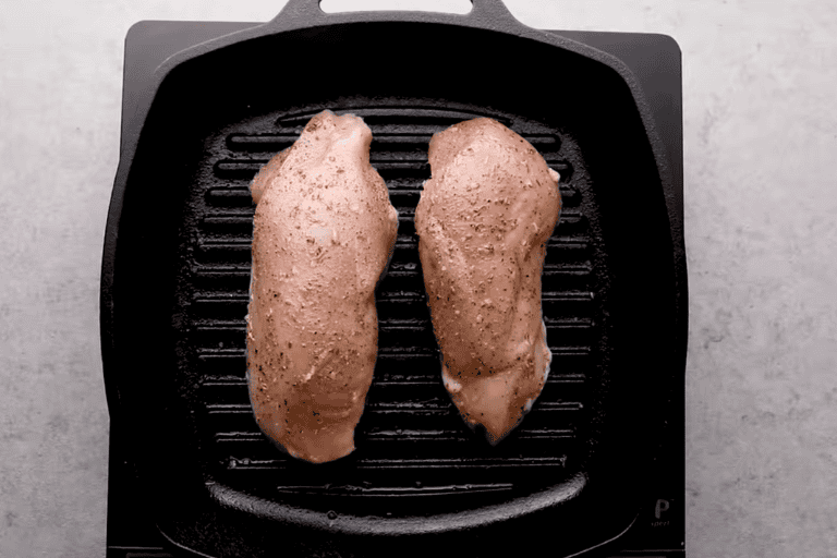 Two seasoned chicken breasts on a grill pan.