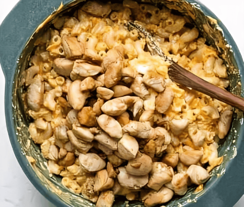 Stirring cooked chicken into a pot of mac and cheese.