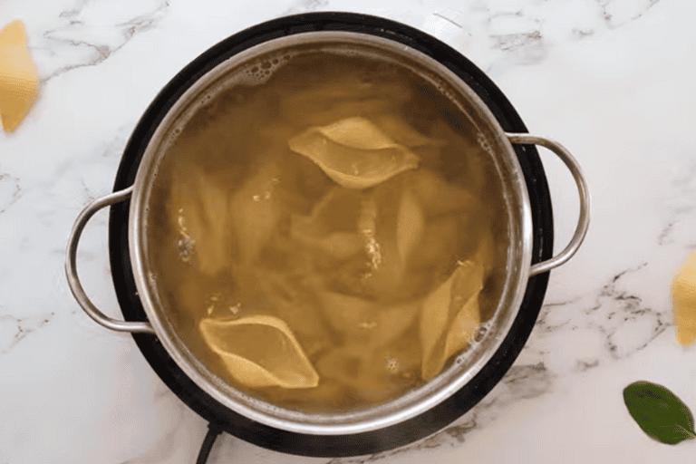 Jumbo pasta shells in boiling water in a pot.