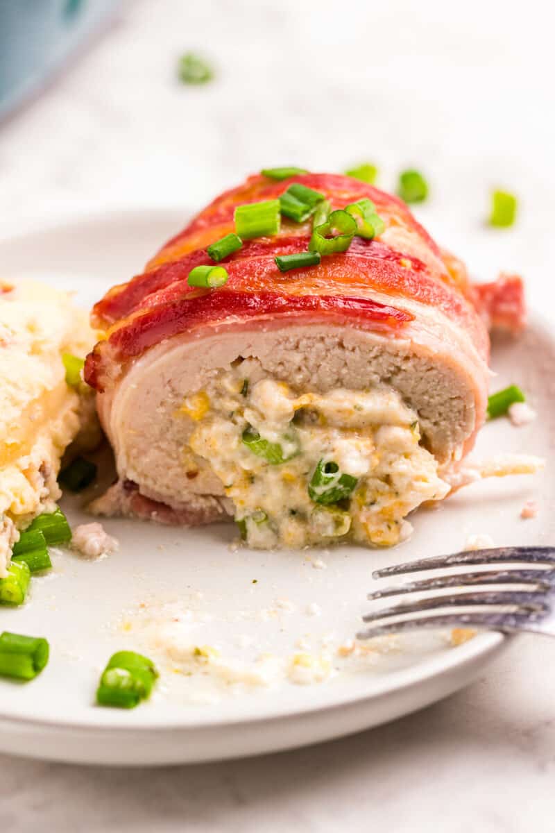 bacon wrapped stuffed chicken on white plate showing inside