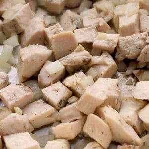 sautéeing cubed chicken with onion in a pan.