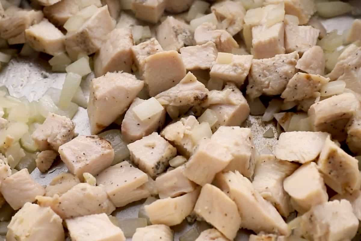 sautéeing cubed chicken with onion in a pan.