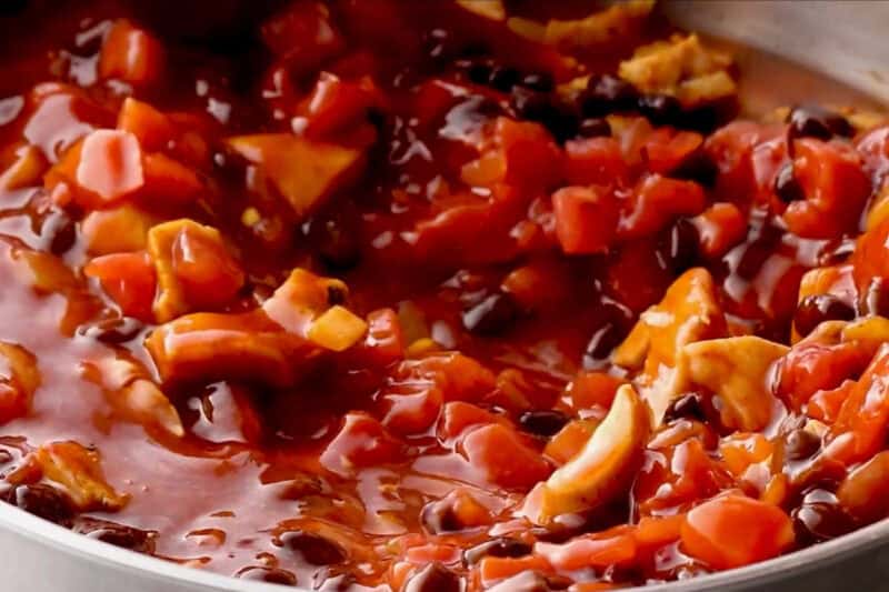 simmering chicken, onions, black beans, tomatoes, and enchilada sauce in a pan.