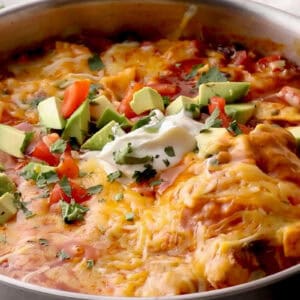 gooey cheese-topped chicken enchilada skillet with avocado, tomato, and sour cream.