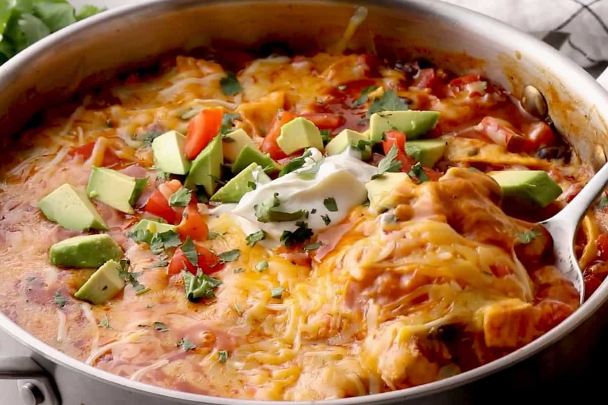 gooey cheese-topped chicken enchilada skillet with avocado, tomato, and sour cream.