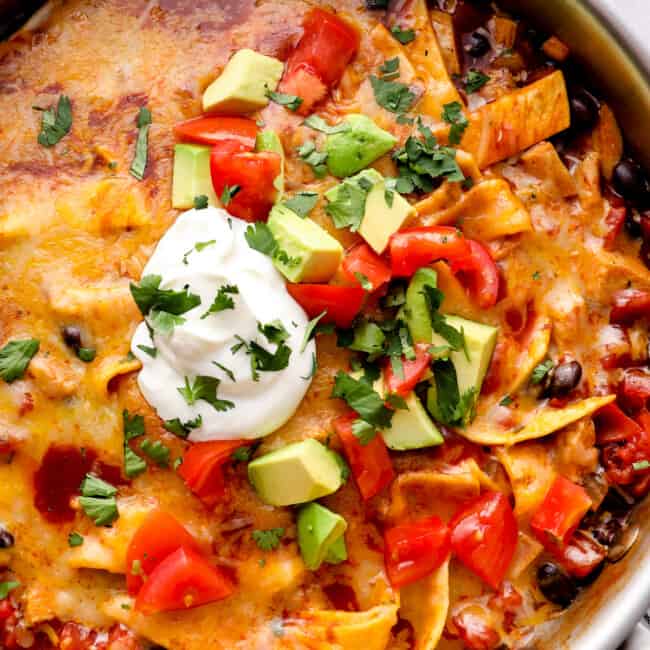 up close chicken enchilada skillet garnished with sour cream, avocado, tomatoes, and cilantro