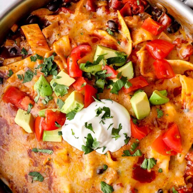 up close chicken enchilada skillet garnished with sour cream, avocado, tomatoes, and cilantro