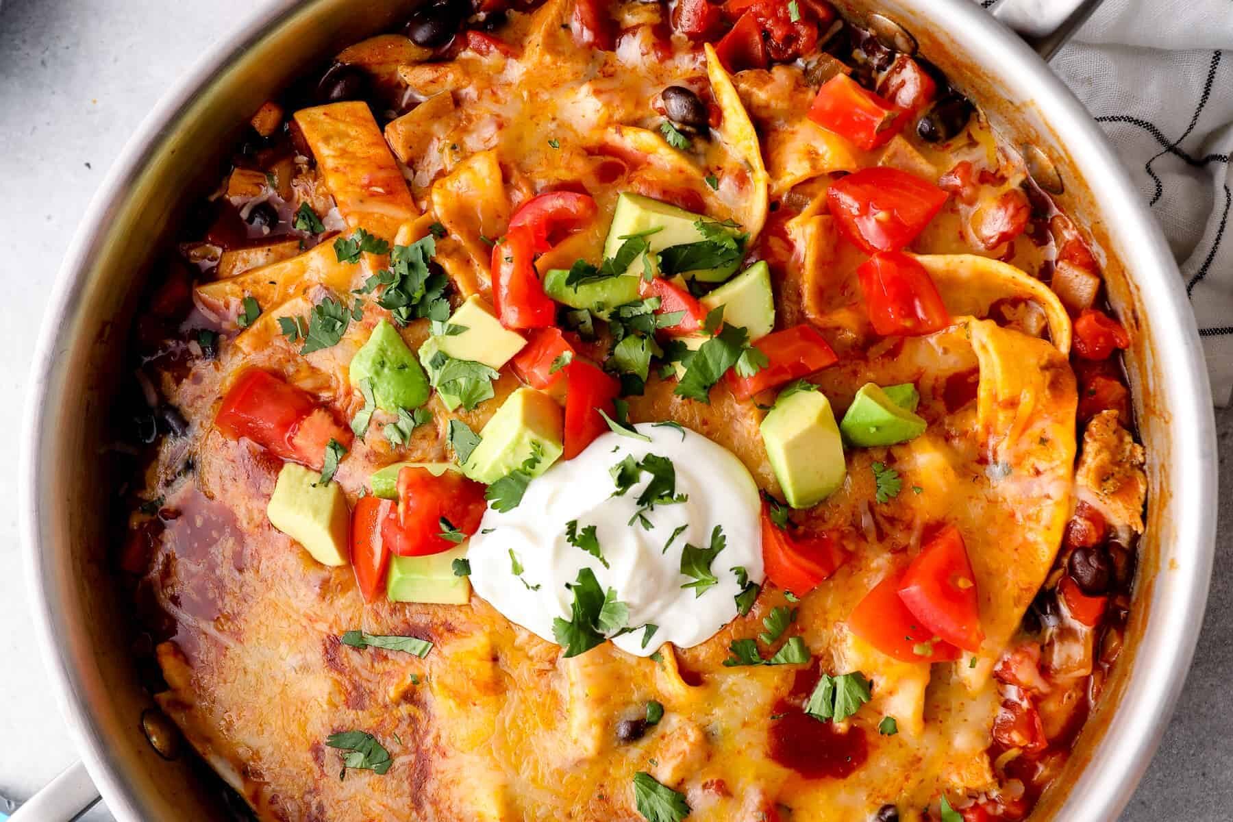 up close chicken enchilada skillet garnished with sour cream, avocado, tomatoes, and cilantro