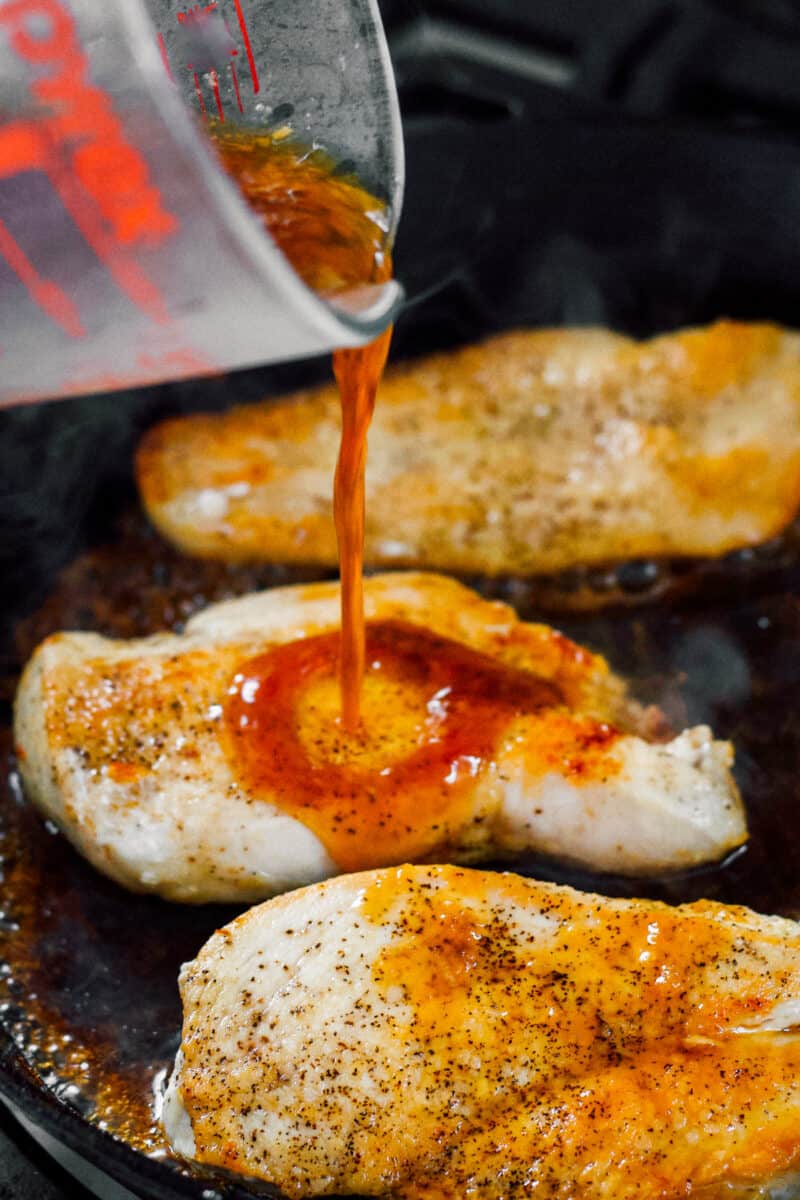 pouring honey garlic sauce over chicken breasts