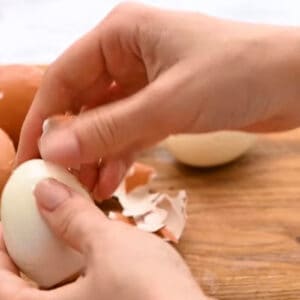 peeling a hard boiled egg on a cutting board.