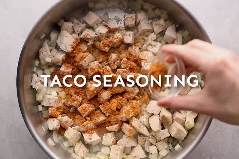 Taco seasoning being poured into a skillet with chicken and onions.