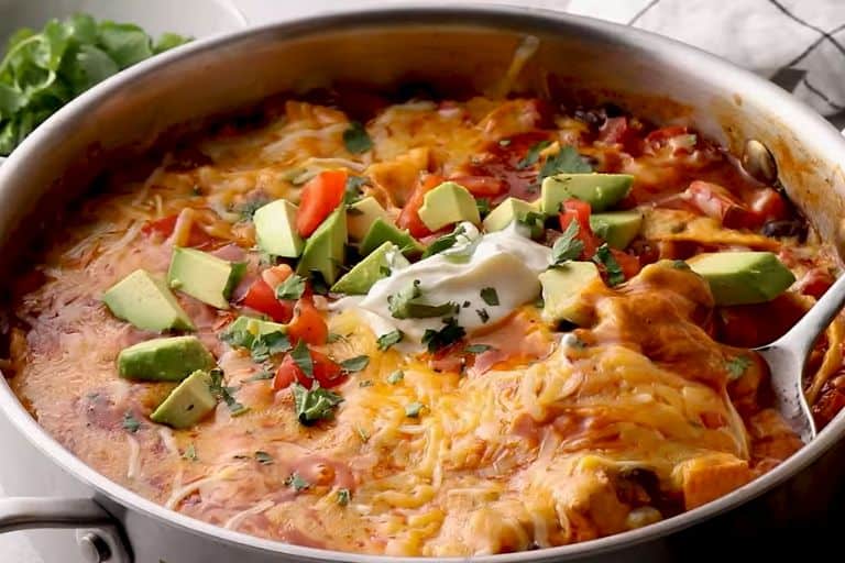 Chicken enchilada casserole topped with avocados, tomatoes, and cilantro in a skillet.