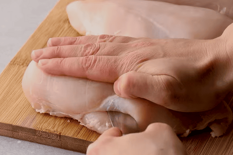 A knife slicing a chicken breast.