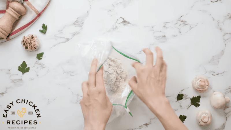 dredging a chicken thigh in flour in a Ziplock bag.