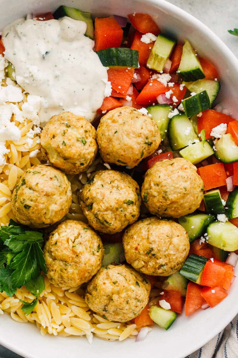 up close Greek chicken meatballs over veggies, rice and tzatziki sauce