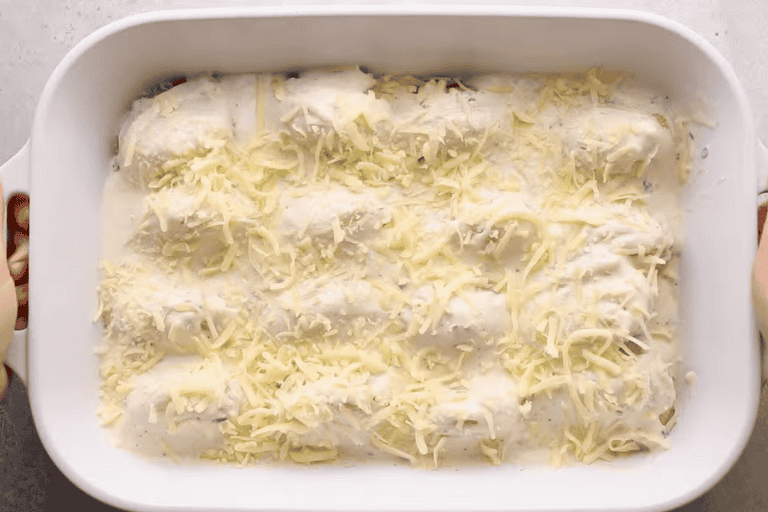 Chicken alfredo stuffed pasta shells in a baking dish topped with cheese.