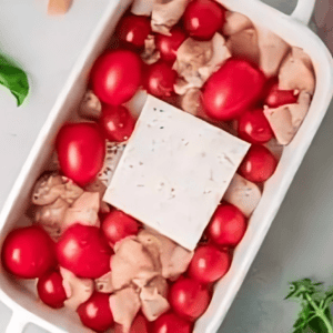 cherry tomatoes, raw chicken, and a block of feta in a baking dish.