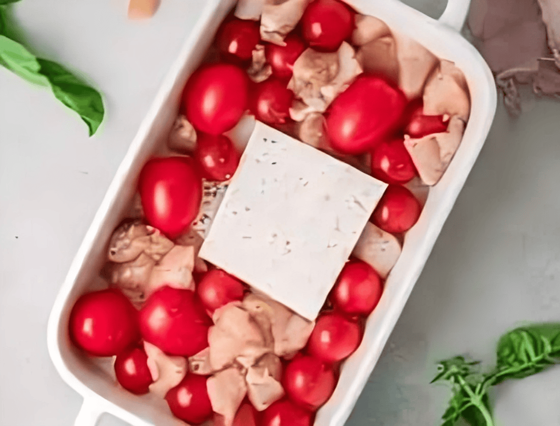 cherry tomatoes, raw chicken, and a block of feta in a baking dish.