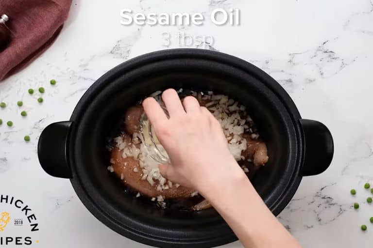 A hand pouring sesame oil on chicken in a crockpot.