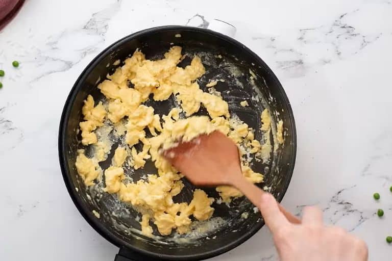 Scrambled eggs in a skillet being stirred with a spatula.