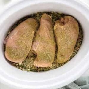 Seasoned chicken breasts in a crockpot with wild rice.