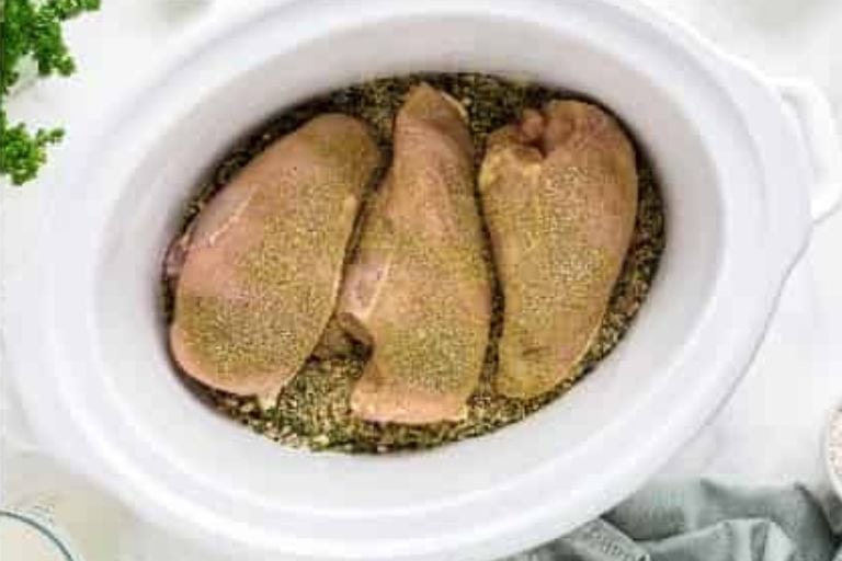 Seasoned chicken breasts in a crockpot with wild rice.