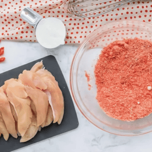 raw chicken tenders on a cutting board and hot cheeto crumbs in a glass bowl.