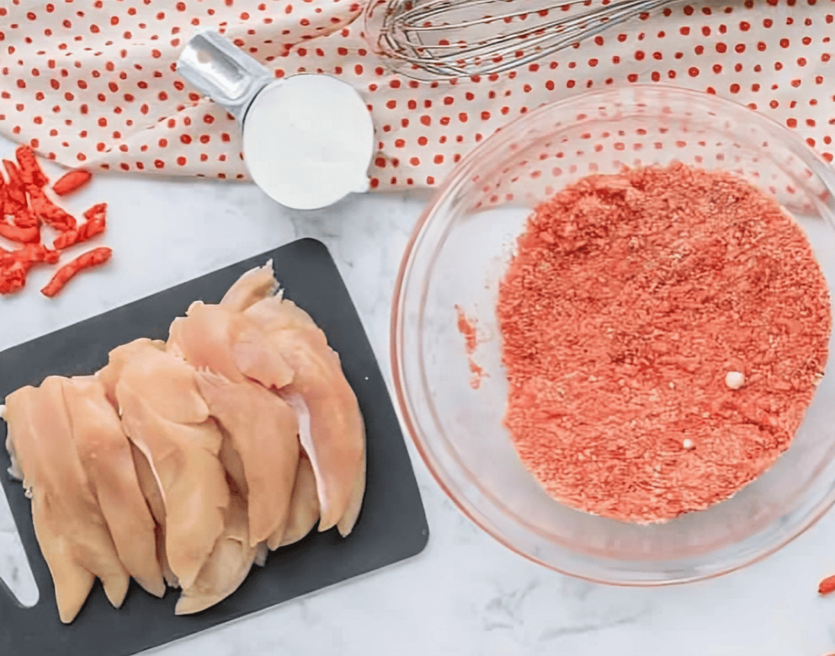 raw chicken tenders on a cutting board and hot cheeto crumbs in a glass bowl.