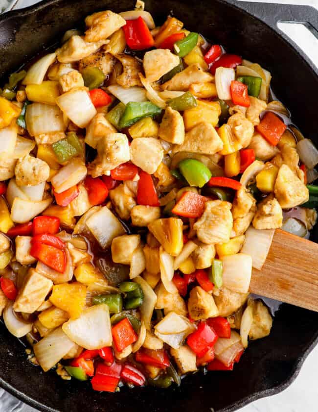 sweet and sour chicken in skillet with wooden spoon